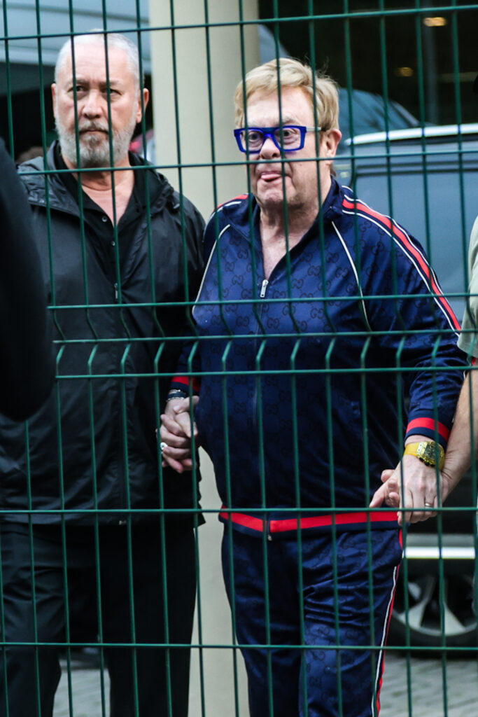 Elton John aparece acompanhado por equipe antes de embarcar