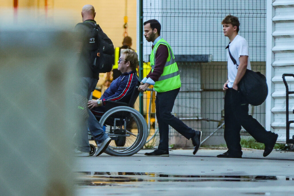 Elton John segue em cadeira de rodas em direção a uma aeronave